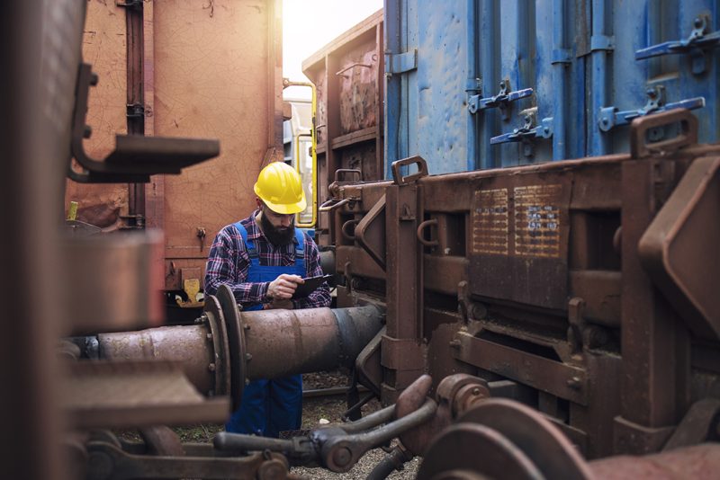 Railroad worker checking on cargo containers at freight train station.